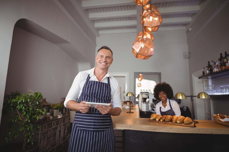 Waiter holding digital tablet while waitress smiling in background at counter in restaurant