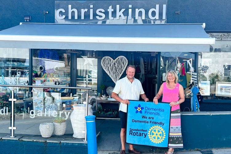 John Walker-Smith, the Treasurer of Tenby Memory Café and lead volunteer in the Dementia Friendly Saundersfoot project, is seen with Lesley displaying the new blue floor mat, kindly supplied by Saundersfoot Rotary Club, which is now in place welcoming customers at Christkindl.