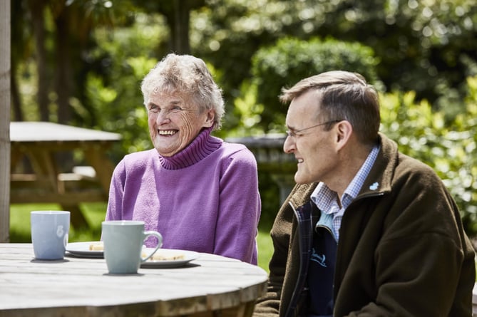 Old lady enjoying tea and cake in outdoors setting with son, male carer or friend.