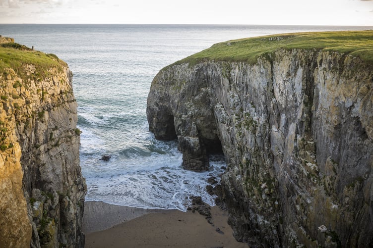 Waves break onto a small beach between two cliffs. Stackpole, Pembrokeshire.