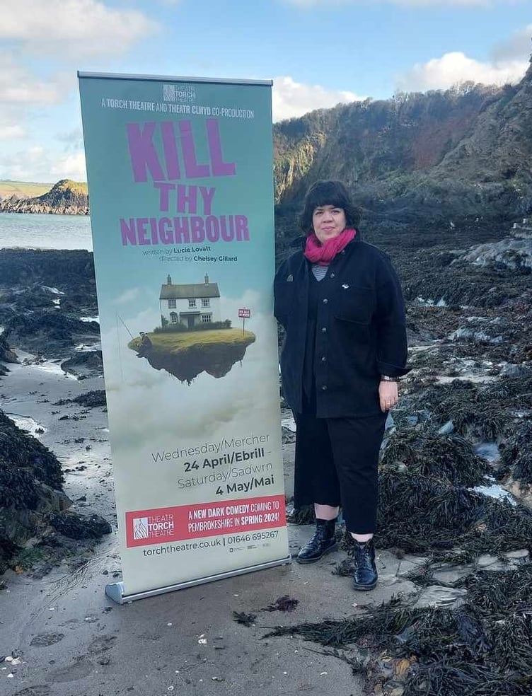 Artistic Director Chelsey Gillard with Kill Thy Neighbour play advertisement on Pembrokeshire beach.