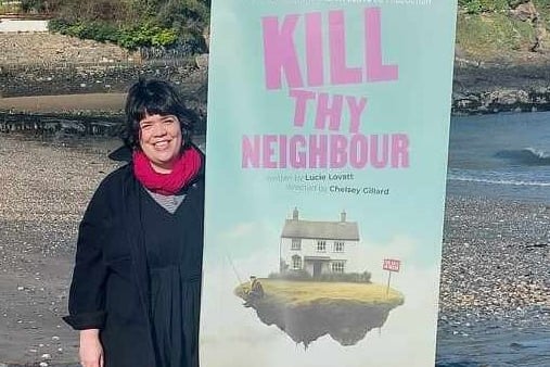 Artistic Director Chelsey Gillard with Kill Thy Neighbour play advertisement on Pembrokeshire beach.