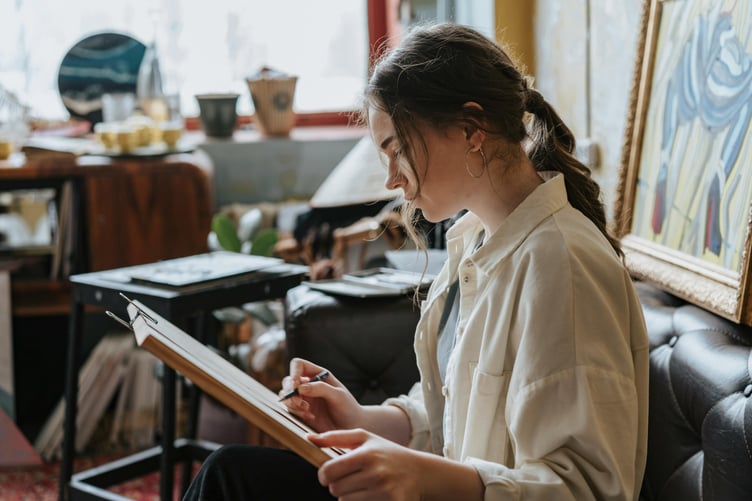 teenage girl sitting on couch using pencil in art studio