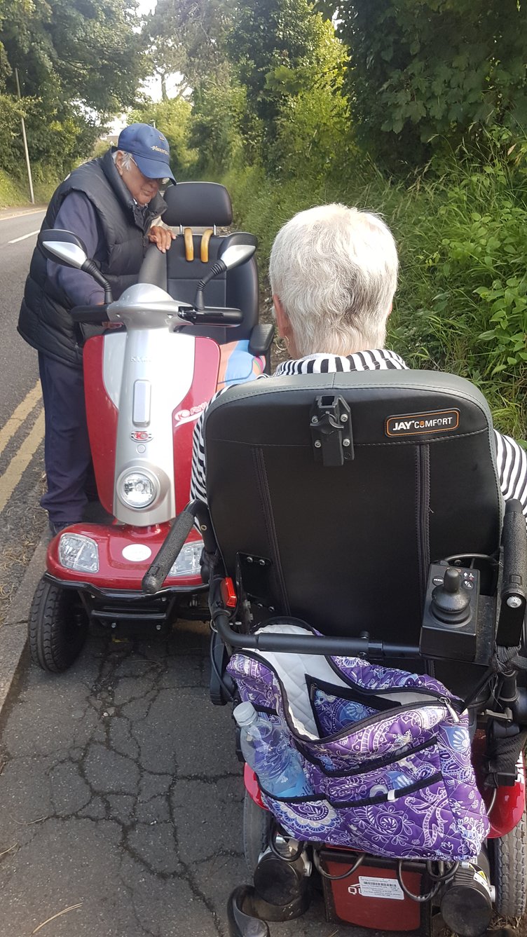 Two mobility aid users struggle to pass each other on a narrow, crazed pavement in Tenby