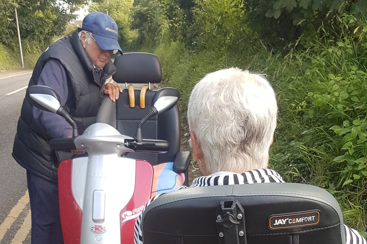 Two mobility aid users struggle to pass each other on a narrow, crazed pavement in Tenby
