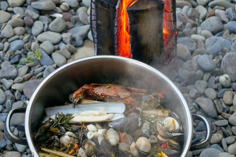 Foraged shells are transformed into a feast, cooked over a Swedish candle made by cutting channels into a single upright log to allow airflow, creating a natural stove for cooking  foraged finds.