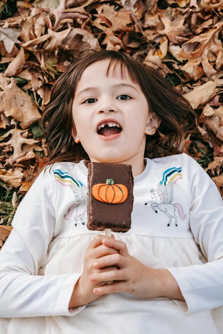 Girl amid autumn leaves about to eat pumpkin lolly