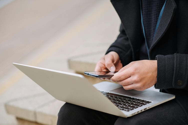 Man sitting outside on steps using laptop and mobile phone
