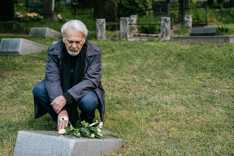 Older man grieving at grave stone