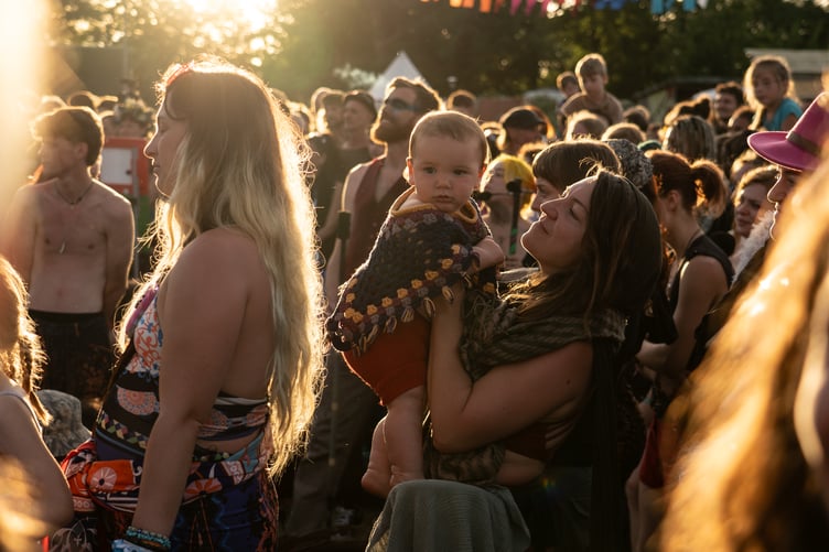A festival-goer soaks up the last of the golden hour sun with her young child as Unearthed draws to a close.