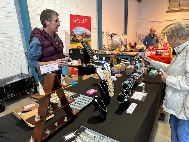 Customer at Caitlin Designs stall in Pembroke Dock Market Hall. The Wales Air Ambulance sign and stall is visible behind.
