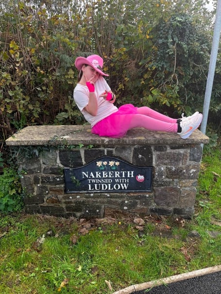 Eleven-year-old Lottie Mills, in pink tutu, gloves, hat and leggings, sitting on the Narberth twinning sign